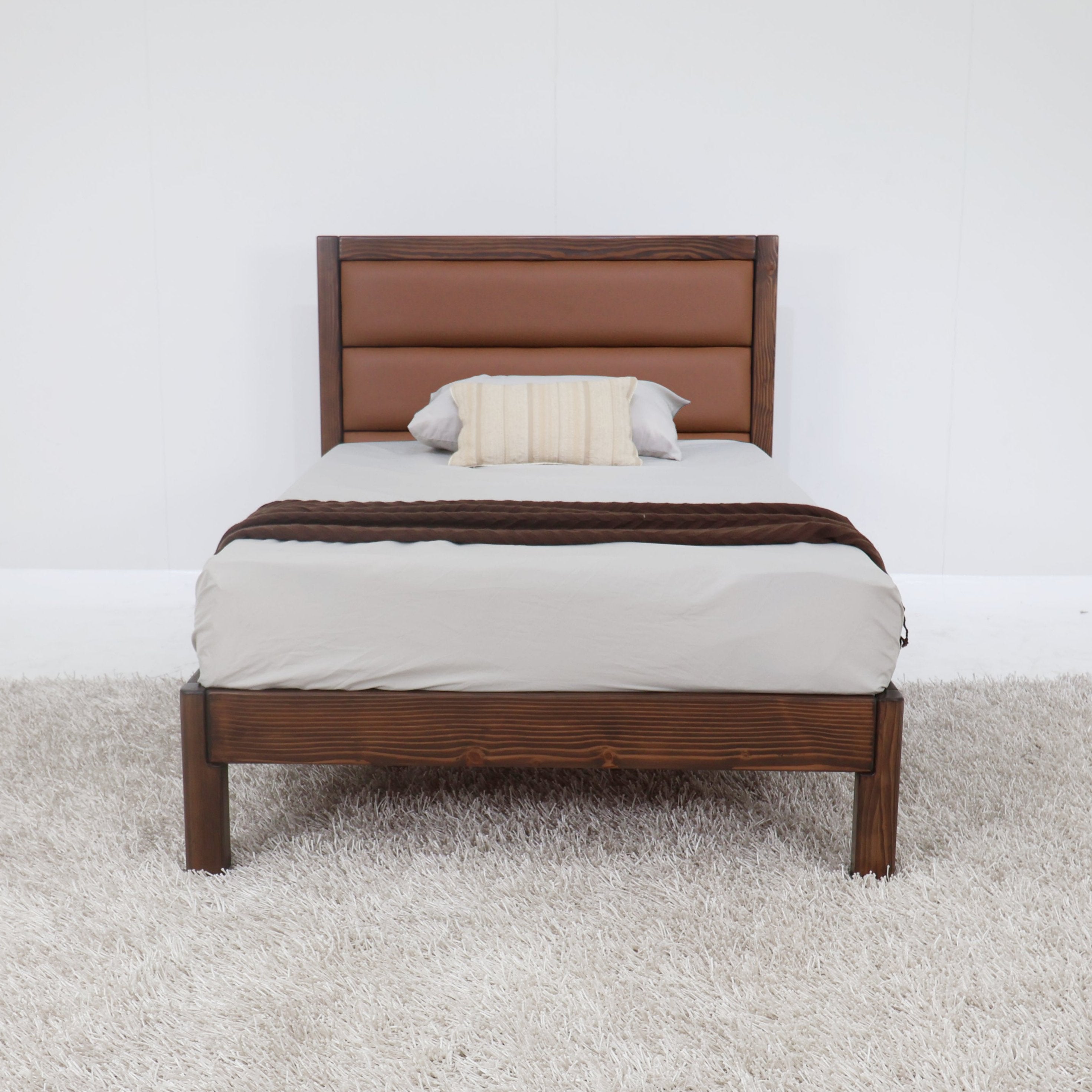 Tan upholstered headboard platform bed with brown wooden frame and bedding