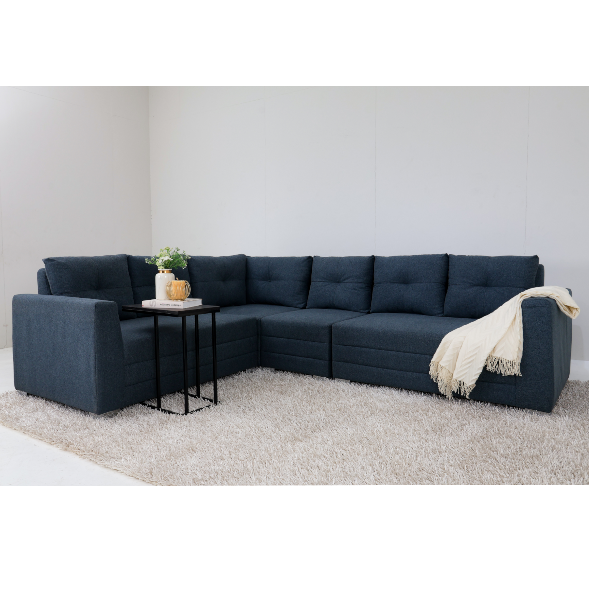 Blue corner sofa with tufted cushions and white block feet, with a throw blanket on arm